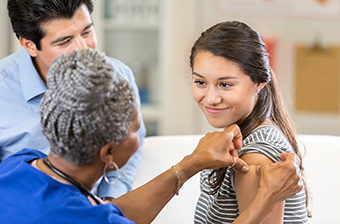 Nurse applying bandaid to teen girl's arm after receiving vaccine